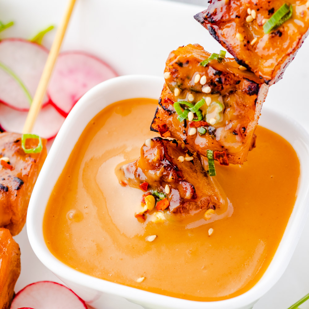 an image of satay on skewers, dipped in a peanut sauce